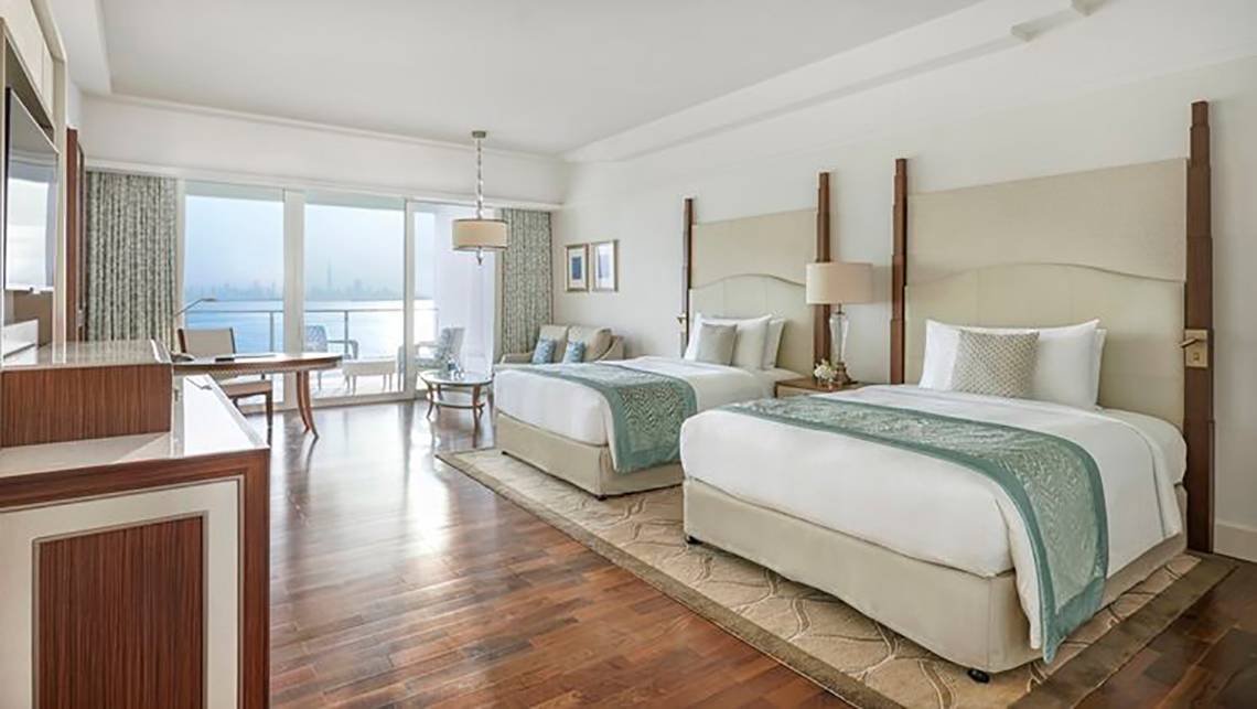 Innenansicht einer Suite im Waldorf Astoria Dubai Palm Jumeirah mit zwei Betten, Schreibtisch und Meerblick.