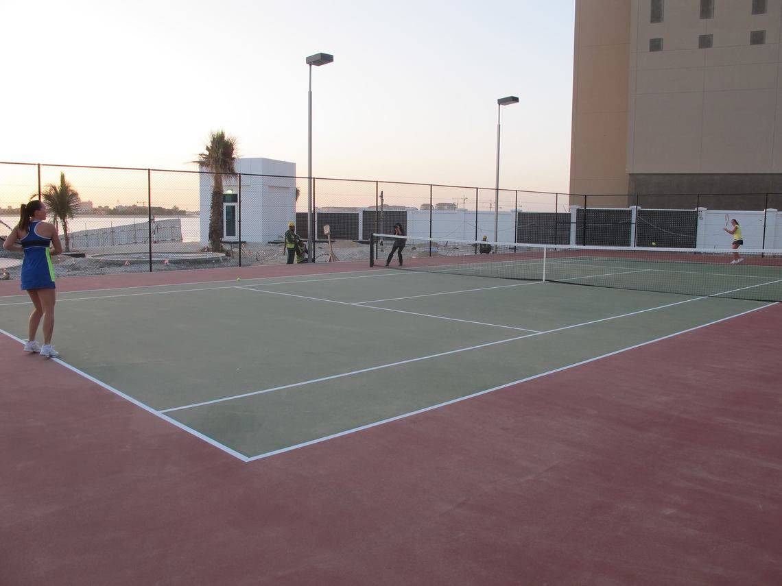 Tennisplatz im Waldorf Astoria Dubai Palm Jumeirah mit Spielern und Arbeitern im Hintergrund.