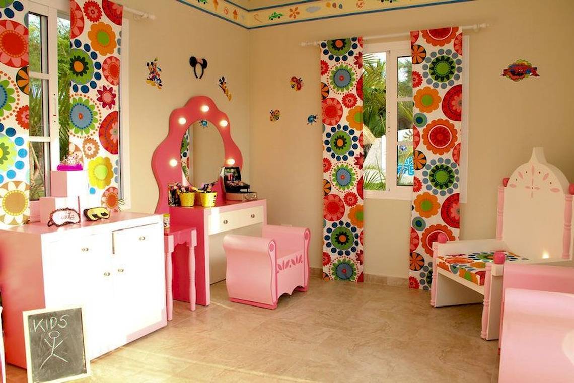 Ein Kinderzimmer mit rosa Möbeln und bunter Blumentapete an den Wänden.