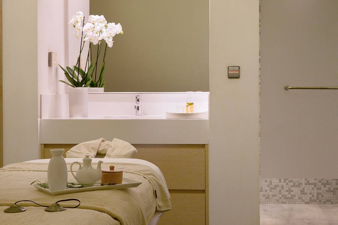 Spa-Behandlungsraum im Capo Bay Hotel mit Tisch, weißen Vasen und Orchideen.