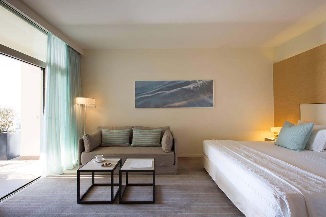 Suite-Zimmer im Capo Bay Hotel mit Blick auf das Meer, einem Bett, einem Sofa und einem Tisch.