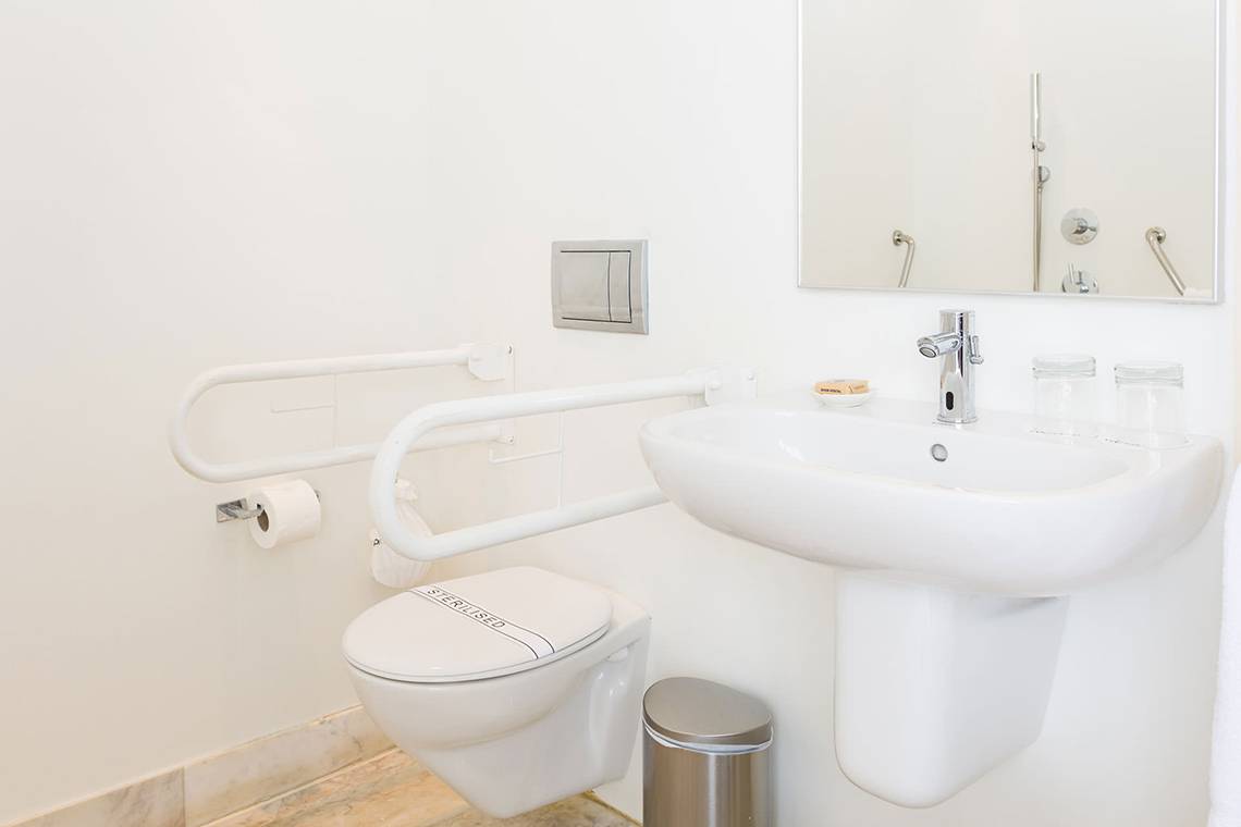 Barrierefreies Badezimmer im Capo Bay Hotel mit Toilette, Waschbecken und Haltegriffen.