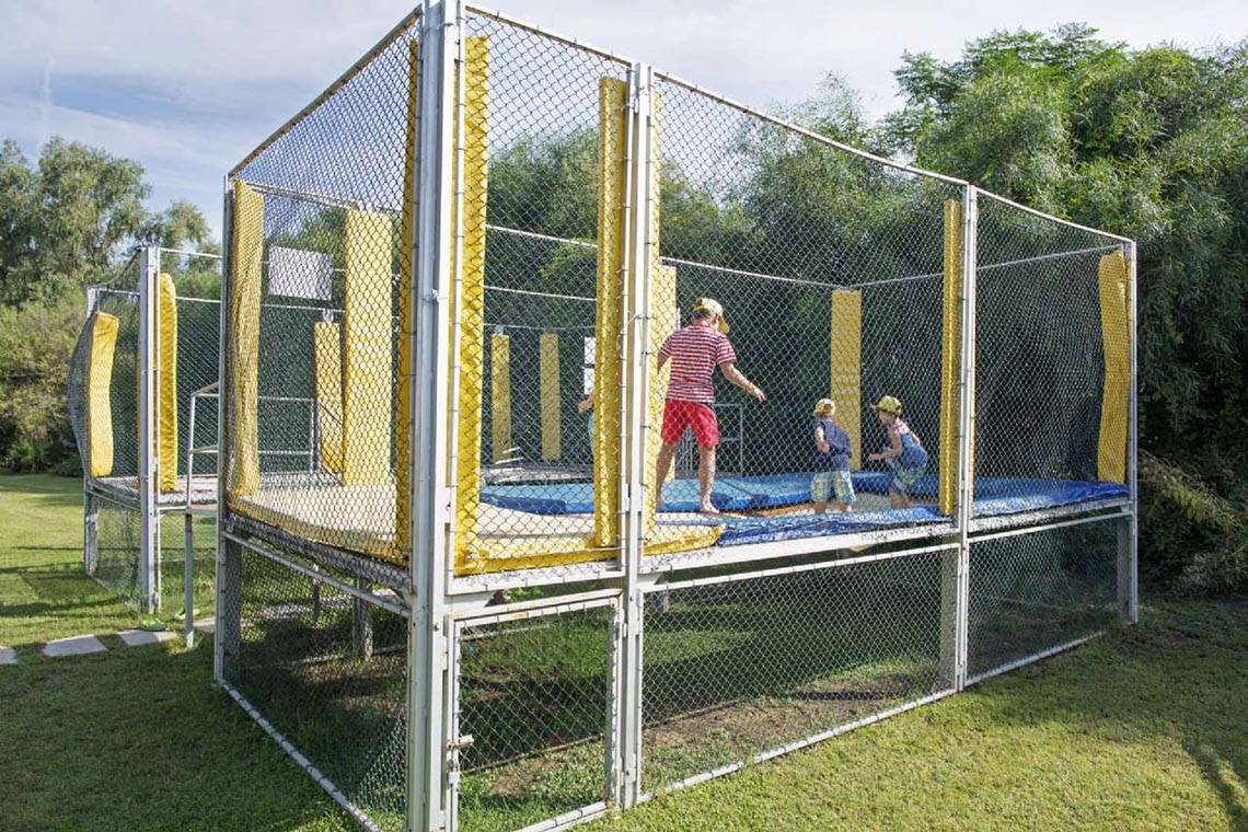 Ein Trampolin-Spielplatz im Freien, umzäunt mit Netzen, mit Kindern, die spielen.