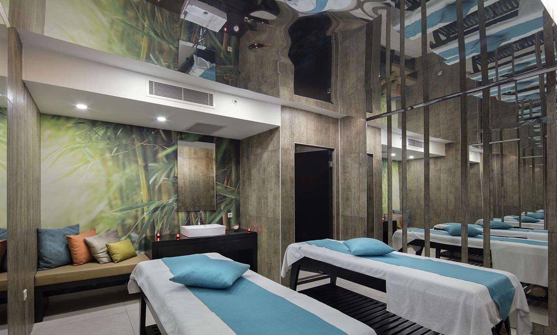 Massageraum im Magic Life Belek Hotel mit blauen und weißen Laken, Kissen und Bambusmotiv an der Wand.