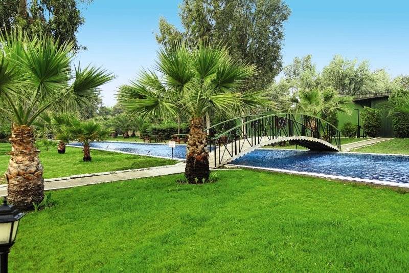 Garten des Palm Wings Ephesus Beach Resorts mit Brücke und Palmen