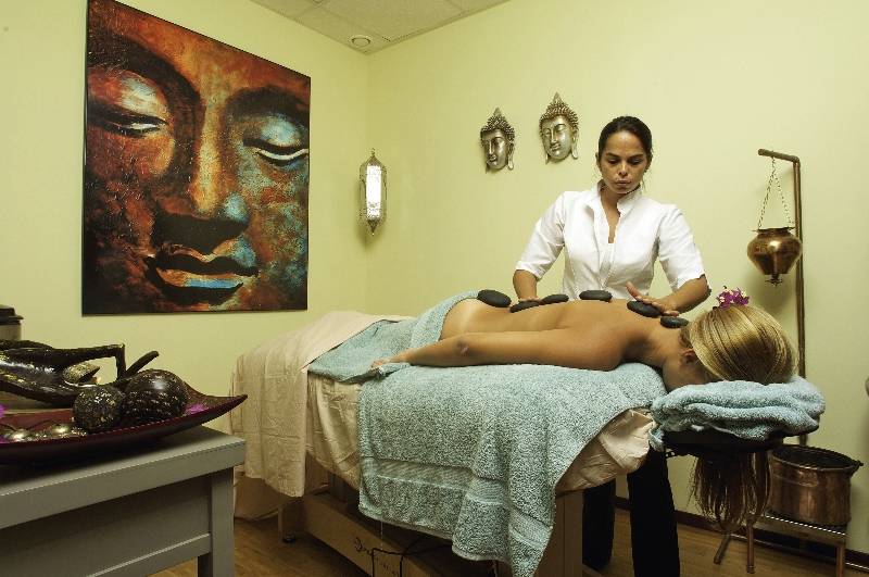 Eine Frau erhält eine Massagebehandlung in einem Raum mit einer Buddha-Wandmalerei und warmem Licht.