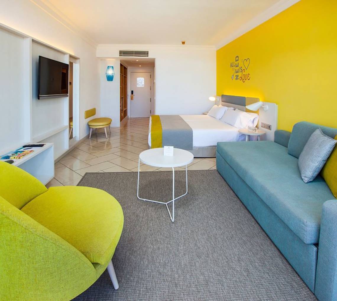 Innenansicht eines Zimmers im Abora Catarina Hotel mit gelber Wand, Doppelbett, Sofa und Tisch.