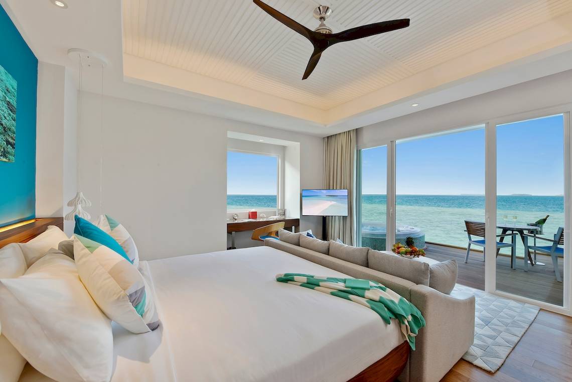 Luxuriöses Hotelzimmer mit Meerblick im Kandima Maldives, mit Kingsize-Bett, Wohnzimmerbereich und Terrasse.