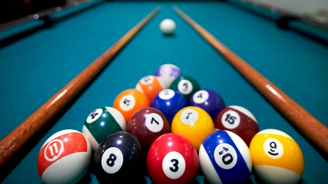 Ein Pooltisch mit bunten Billardkugeln und zwei Keulen, die Kugel Nummer 15 wird angespielt.