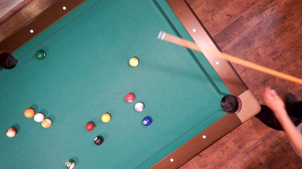 Ein Blick von oben auf einen Pooltisch mit bunten Kugeln und einem Stock.