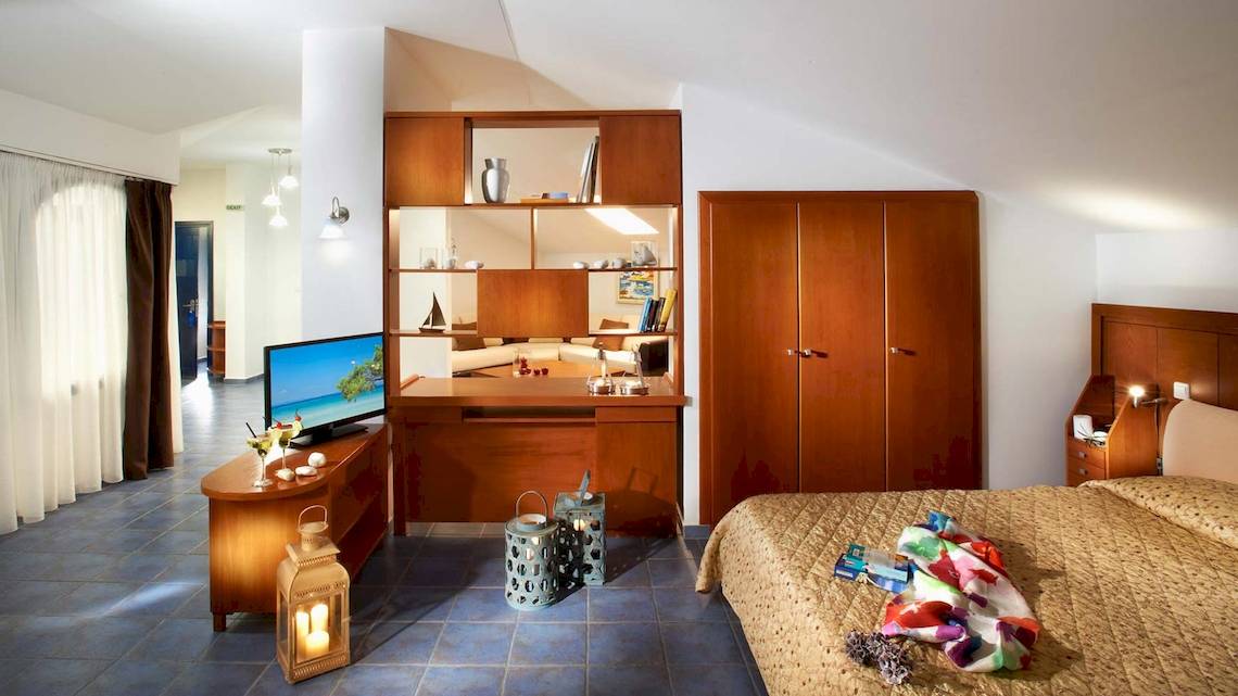 Innenansicht eines Hotelzimmers im Acrotel Athena Pallas, mit Bett, Fernseher, Schrank und Dekor.