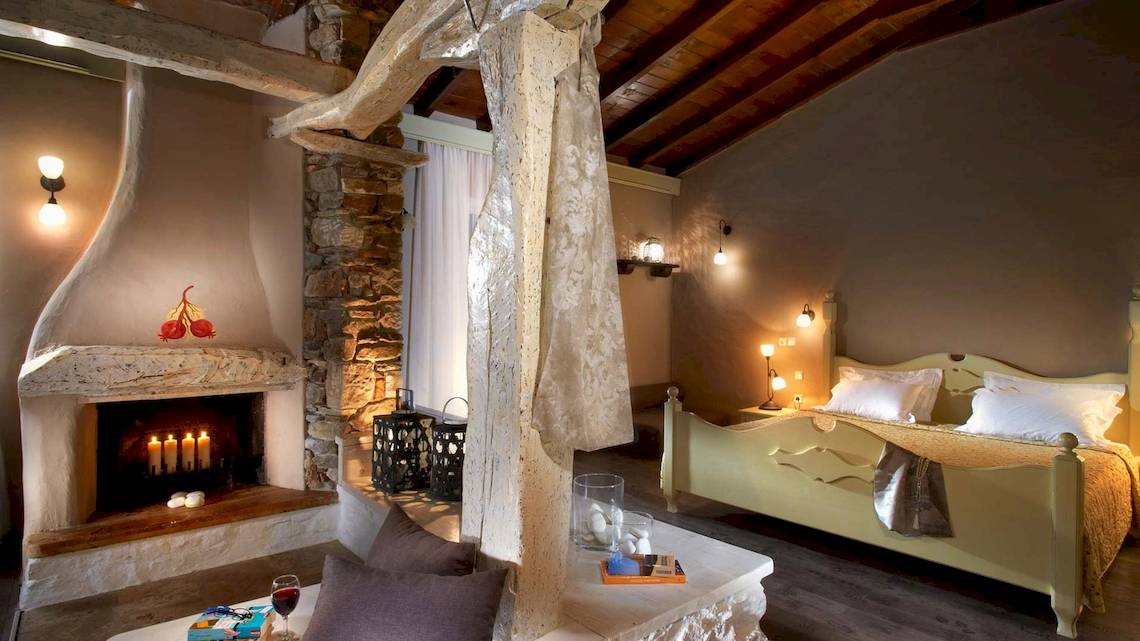 Schlafzimmer im Acrotel Athena Pallas mit Bett, Kamin, Kerzen und Leselampe.