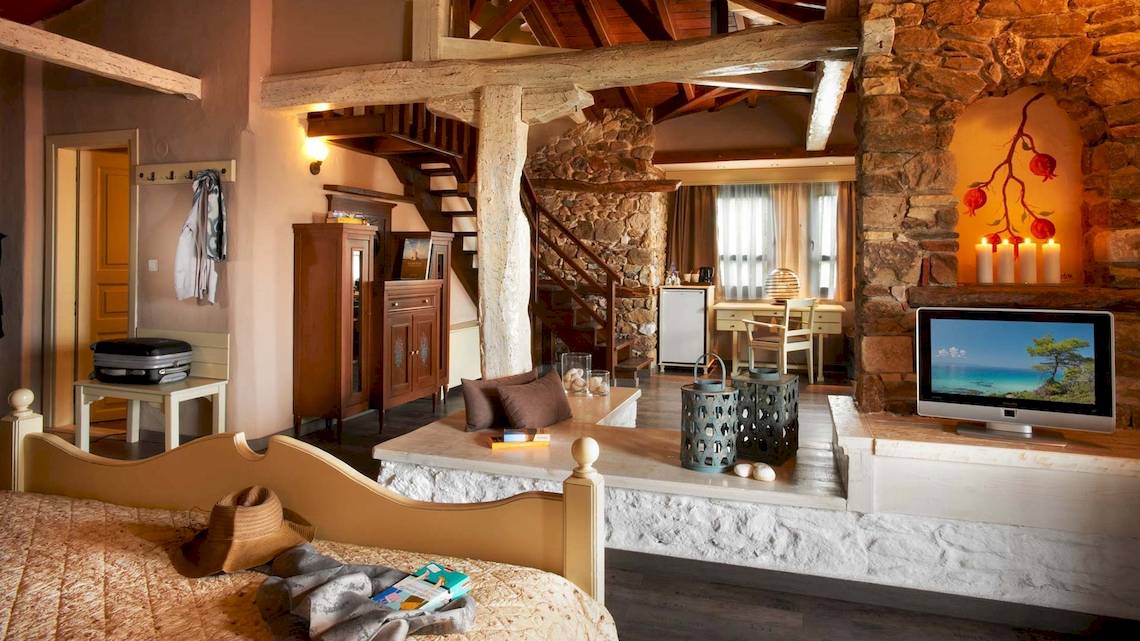 Innenansicht des Acrotel Athena Pallas Hotelzimmers mit Bett, Wohnzimmerbereich und Fernseher.
