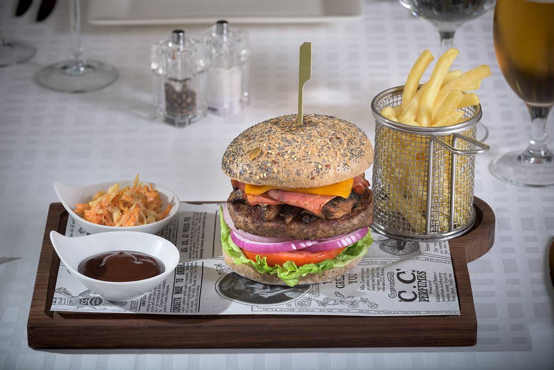 Ein Burger auf einem Holztablett mit Pommes und Getränken im Elysium Resort & Spa.