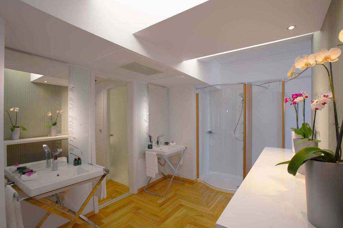 Elysium Resort & Spa Badezimmer mit Dusche, Waschbecken und Orchideen.