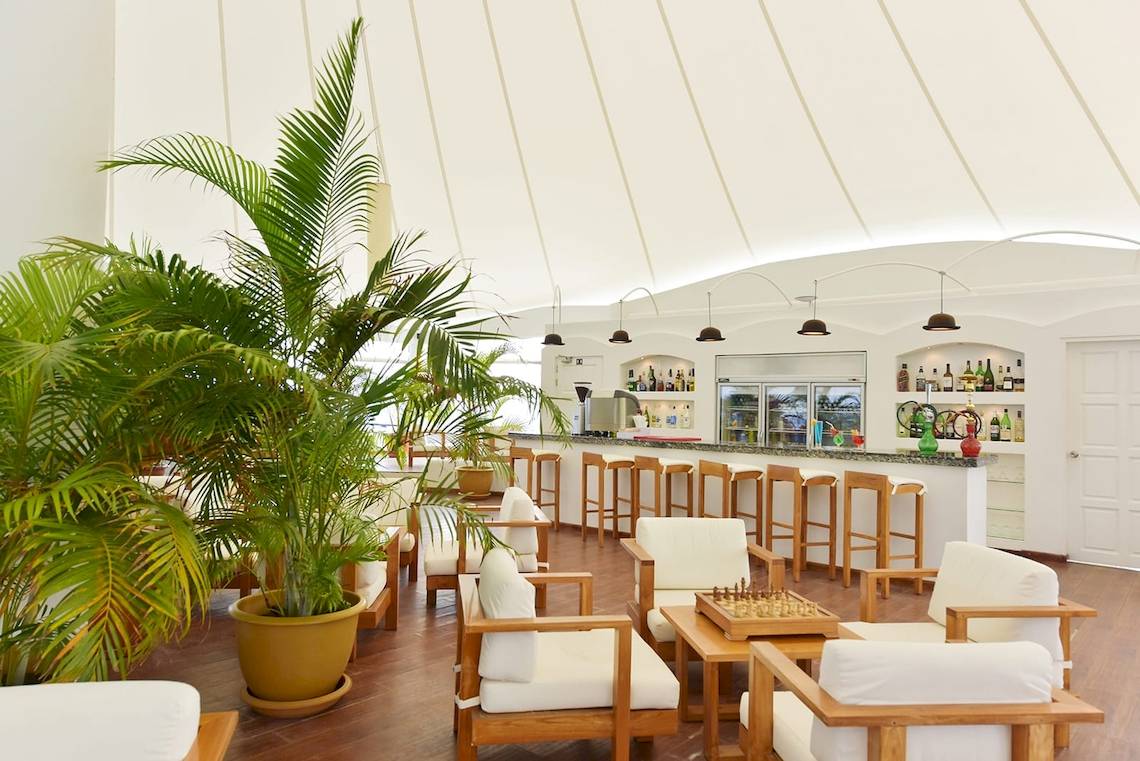 Lounge-Bereich im Safari Island Resort mit weißen Stühlen, Holztischen und Pflanzen.