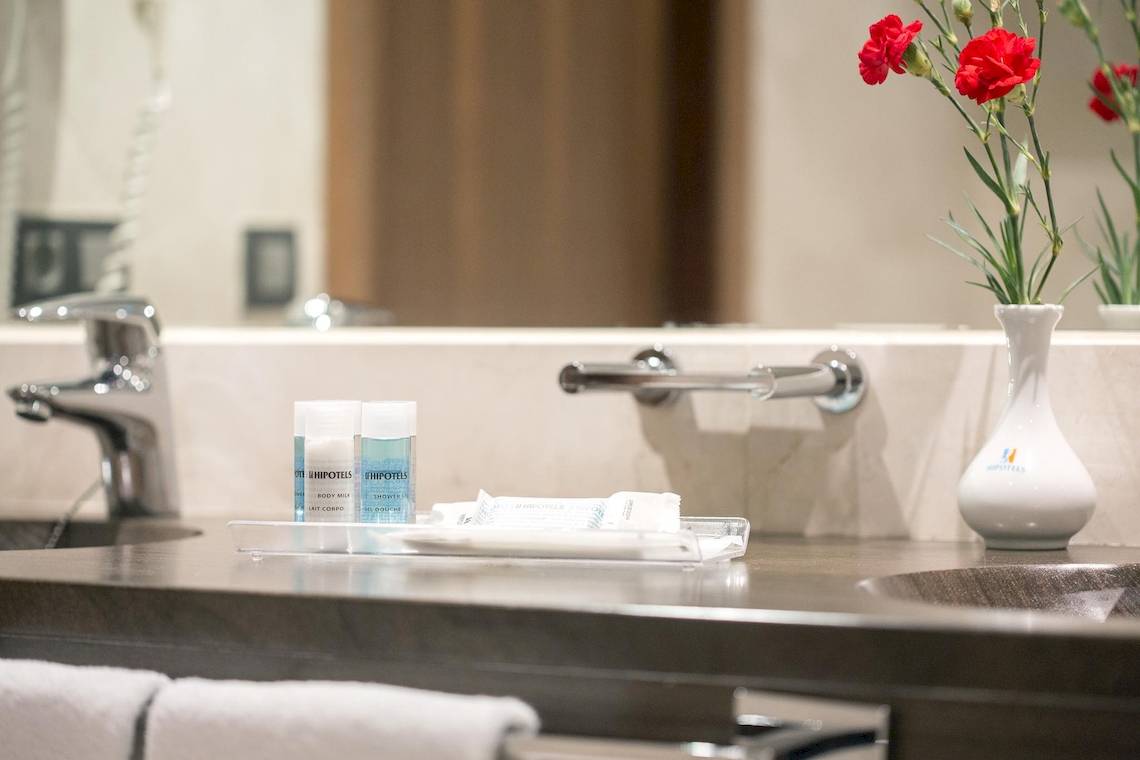 Badezimmer im Hipotels Cala Millor Park Hotel mit Waschbecken, Handtüchern und roten Blumen.