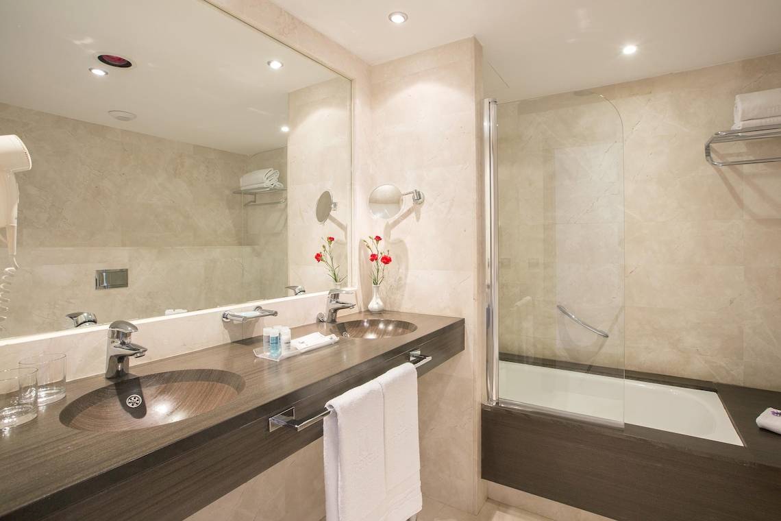 Ein elegantes Badezimmer im Hipotels Cala Millor Park mit zwei Waschbecken, einem Spiegel und einer Dusche.