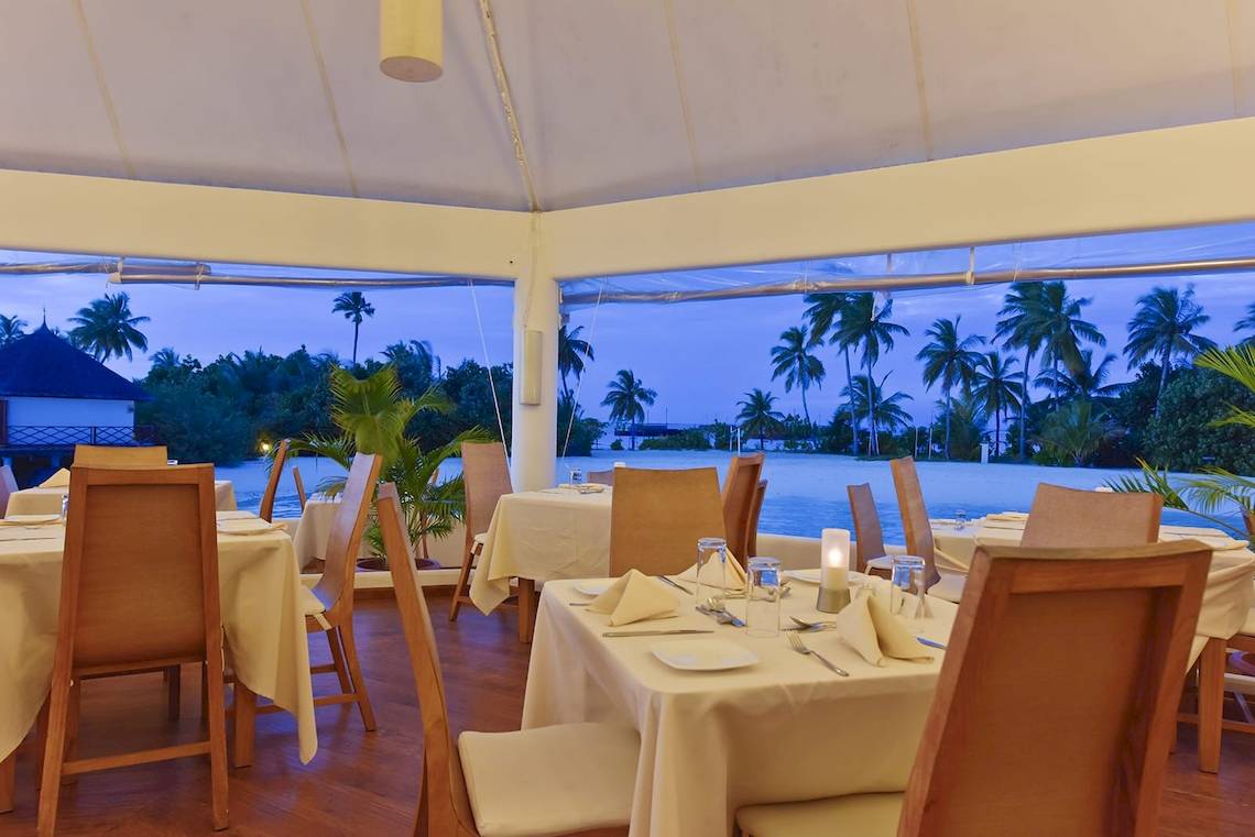 Innenbereich des Restaurants im Safari Island Resort mit Blick auf Palmen und Wasser.