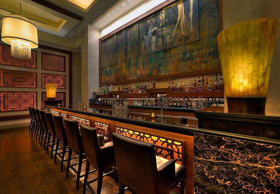 Bar im St. Regis Saadiyat Island Resort mit Barhockern, Theke und dekorativen Wandleuchten.