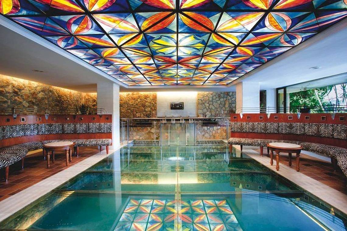Innenpool des Playa Golf Hotels mit bunter Glasdecke und Zebramuster-Bänken
