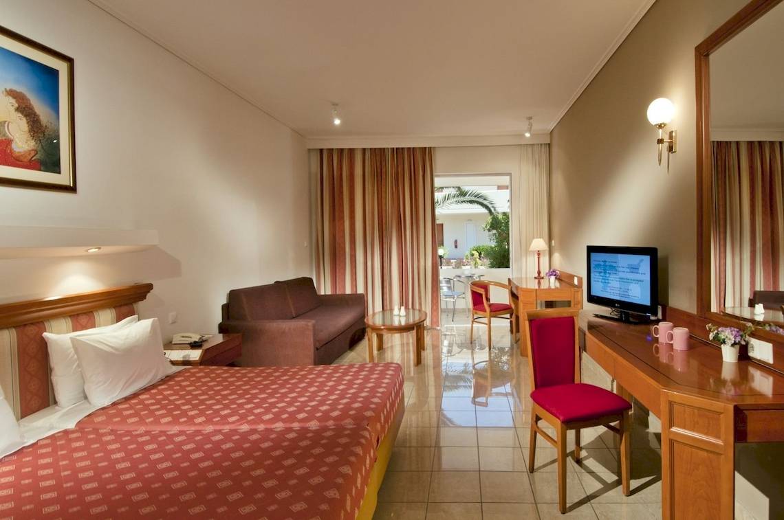 Innenansicht eines Hotelzimmers im Kipriotis Village Resort mit Doppelbett, Sofa, Fernseher und Schreibtisch.
