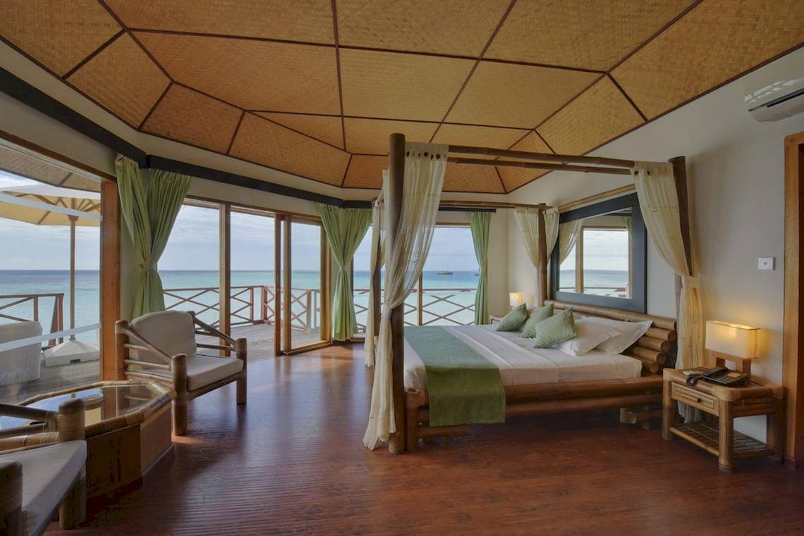 Innenansicht einer Suite im Safari Island Resort mit Meerblick, großes Bett mit Vorhängen, Möbel und offene Terrasse.