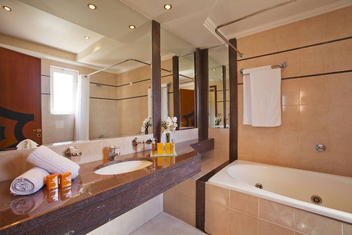 Badezimmer im Kipriotis Village Resort mit Spiegel, Waschbecken und Badewanne.