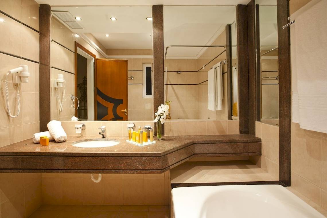 Badezimmer im Kipriotis Village Resort mit Waschbecken, Spiegel und Badewanne.
