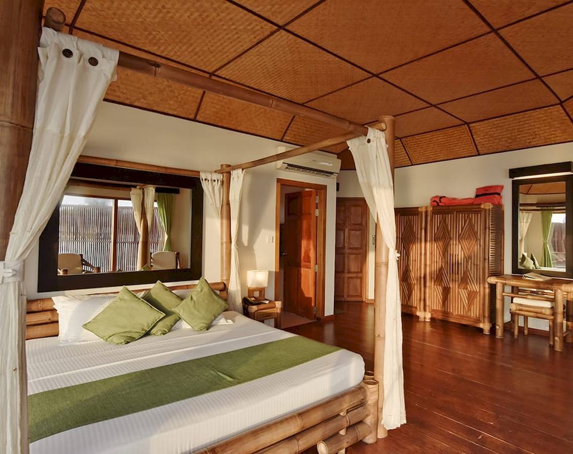 Schlafzimmer im Safari Island Resort mit Himmelbett, grünen Kissen und Holzboden.