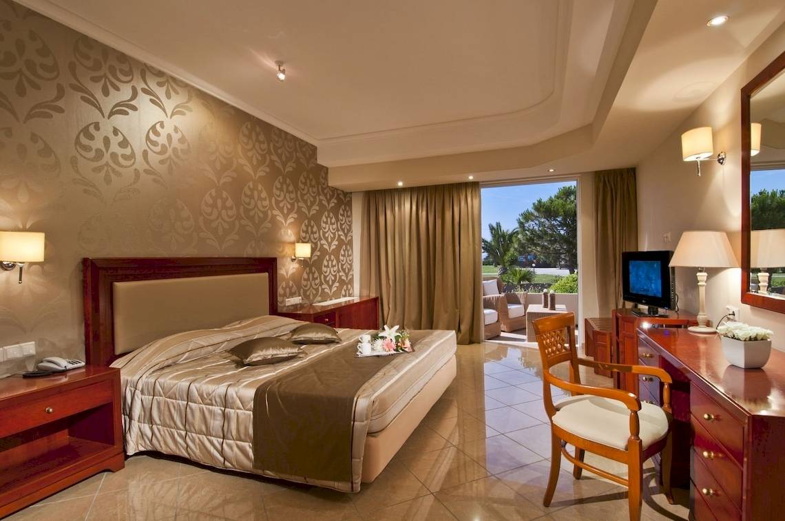 Ein elegantes Hotelzimmer im Kipriotis Village Resort mit Doppelbett, Fernseher, Schreibtisch und Balkon.