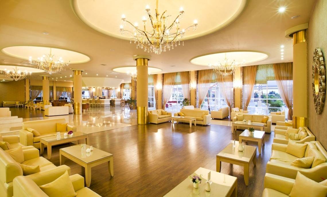 Lobby des Kipriotis Village Resorts mit goldenen Kronleuchtern und cremefarbenen Sofas.