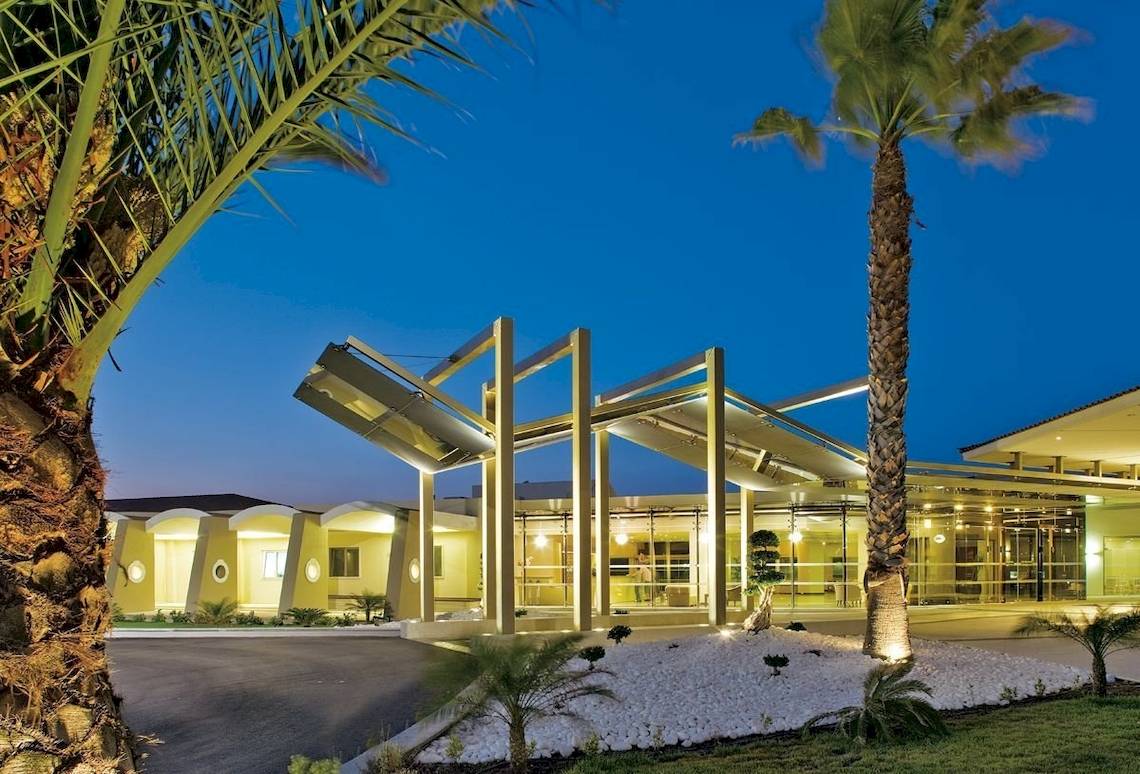 Außenansicht des Kipriotis Village Resort Hotels bei Nacht mit Palmen und Lichtern.