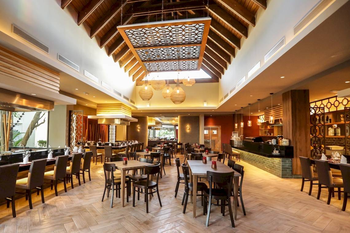 Innenraum des Restaurants im Vista Sol Punta Cana Beach Resort & Spa mit geometrischen Deckenleuchten und Holzboden.