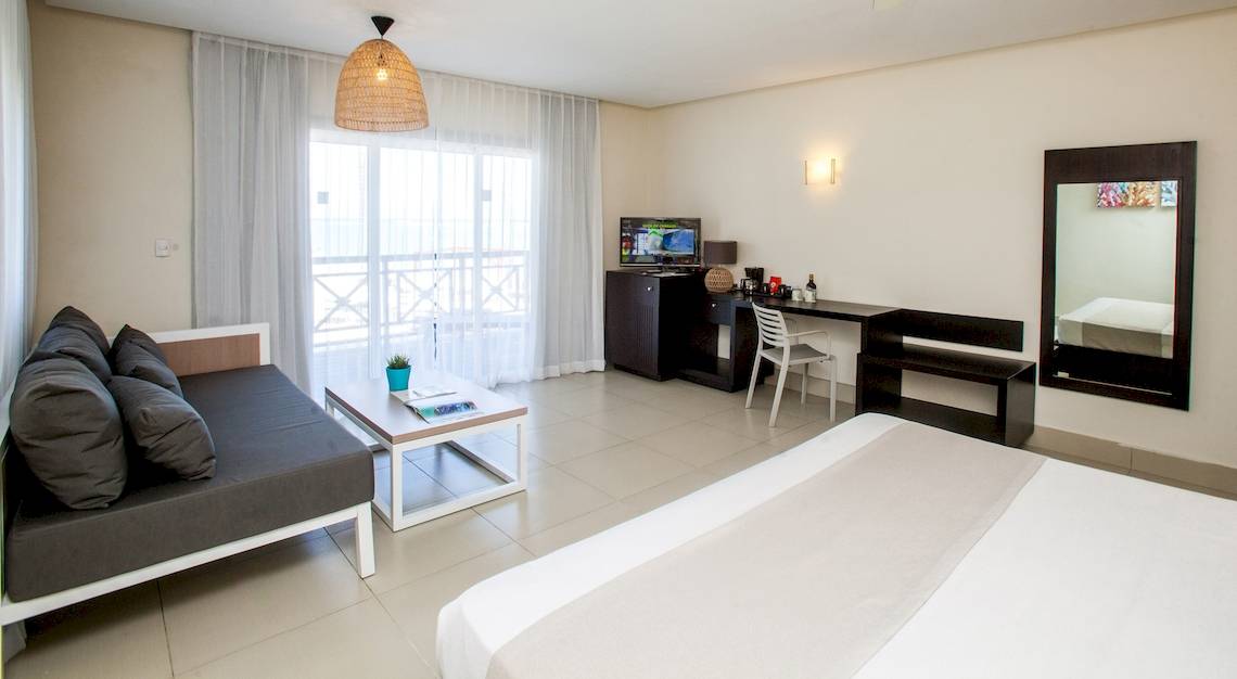 Innenansicht eines Zimmers im Vista Sol Punta Cana Beach Resort mit einem Bett, einem Schreibtisch, einem Fernseher und einem Fenster.