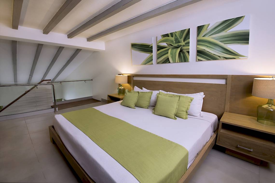 Ein Schlafzimmer im Vista Sol Punta Cana Beach Resort & Spa mit einem großen Bett, grünen Kissen und weißen Decken.