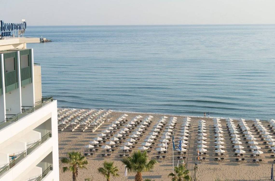 Aussicht auf den Strand vom Aquila Porto Rethymno Hotel, viele weiße Sonnenschirme und Palmen.