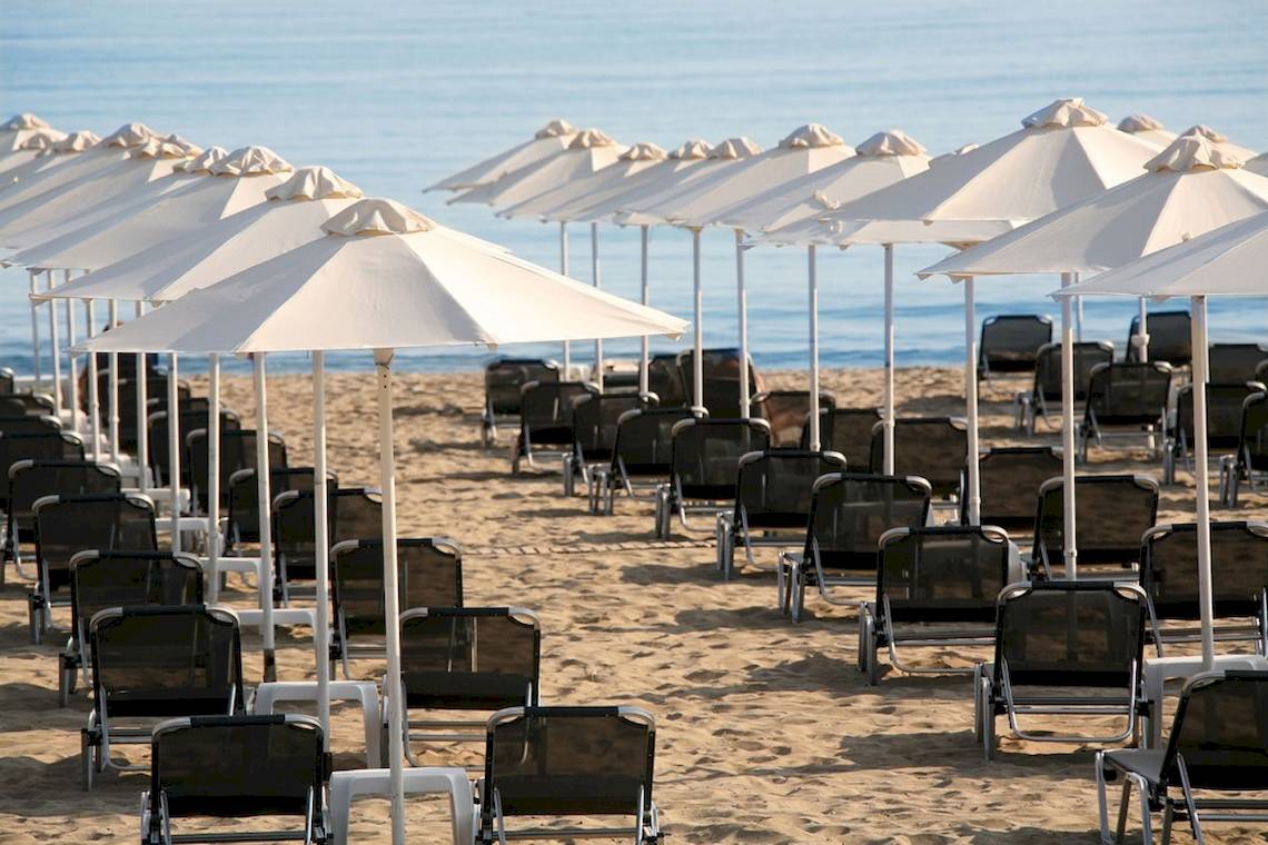 Strand der Aquila Porto Rethymno Hotel mit vielen Sonnenschirmen und Lounge-Stuhle