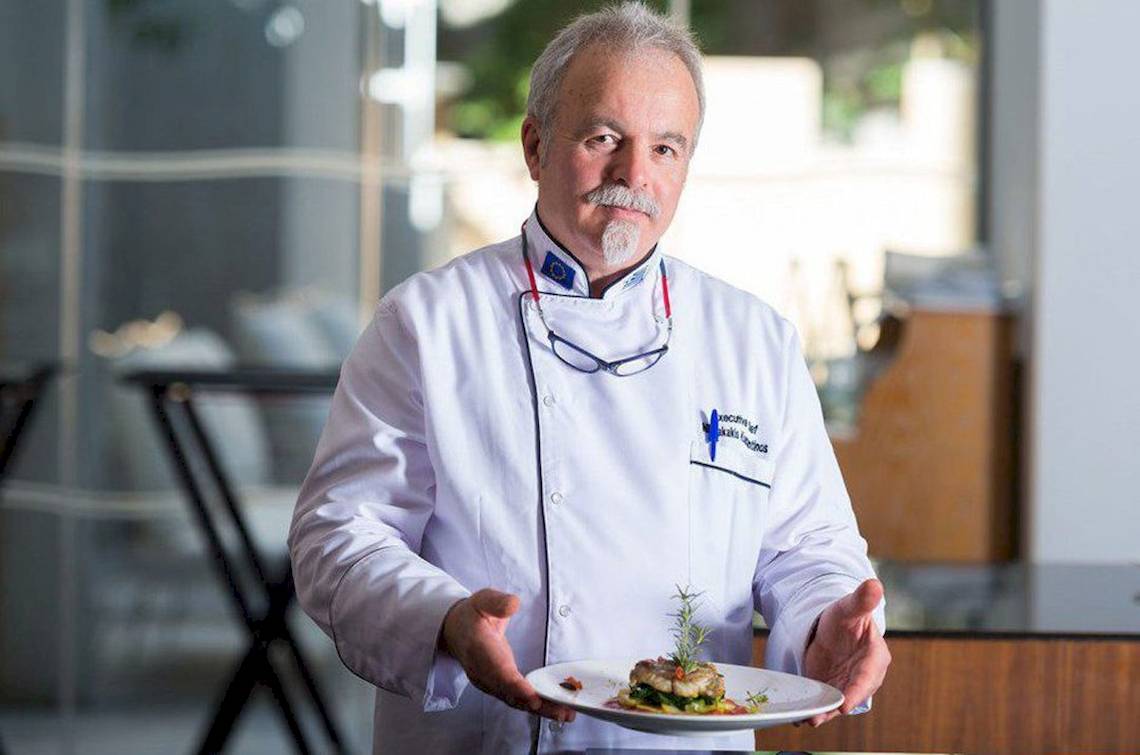 Chef des Aquila Porto Rethymno präsentiert ein Gericht in einem weißen Kochmantel.