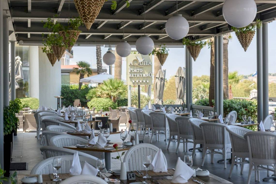 Außenbereich des Aquila Porto Rethymno Hotels mit weißen Stühlen und Tischen.