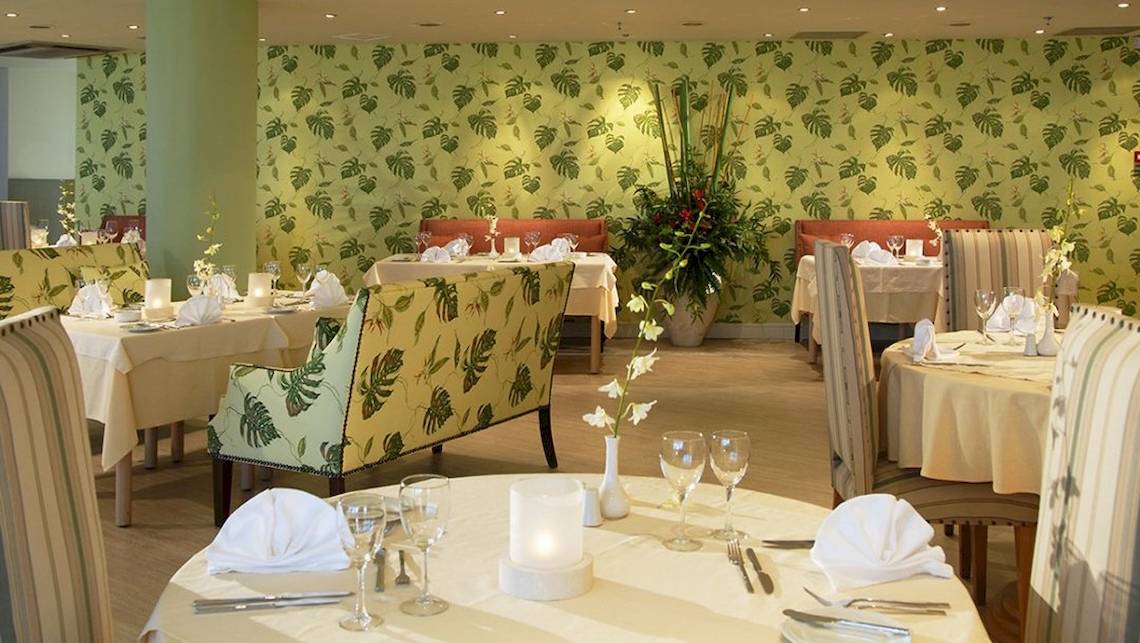 Innenansicht des Restaurants im Aquila Porto Rethymno Hotel mit grün gemusterten Wänden und gedeckten Tischen.