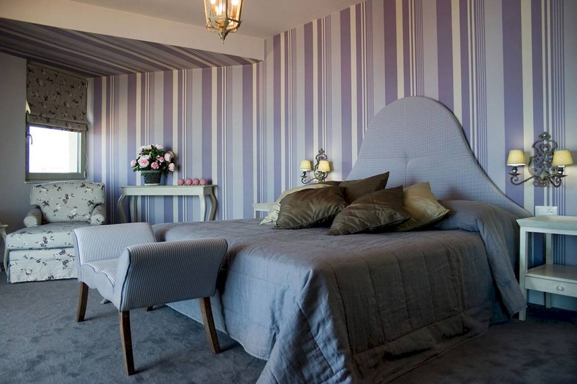 Schlafzimmer im Aquila Porto Rethymno Hotel mit blauen und weißen gestreiften Wänden, einem Bett und einem kleinen Beistelltisch.