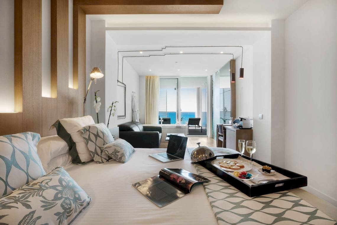 Ein elegantes Hotelzimmer im Pure Salt Garonda mit einem Bett, Laptop und Meerblick.