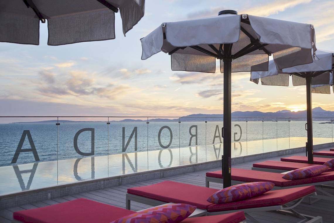 Außenbereich des Pure Salt Garonda Hotels mit roten Sonnenliegen und Sonnenschirmen am Pool.