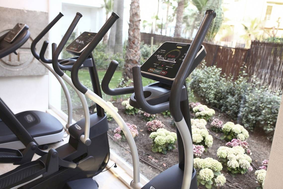 Fitnessgeräte im Pure Salt Garonda Hotel neben einem Garten mit Blumen.