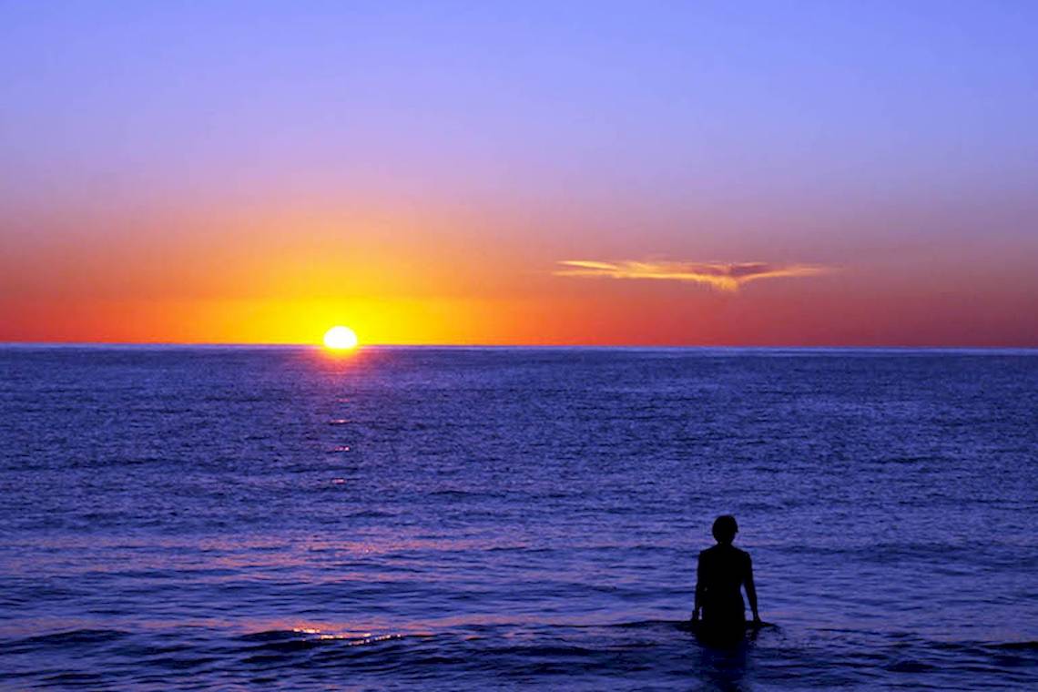 Ein Mensch steht im Meer und beobachtet den Sonnenuntergang.