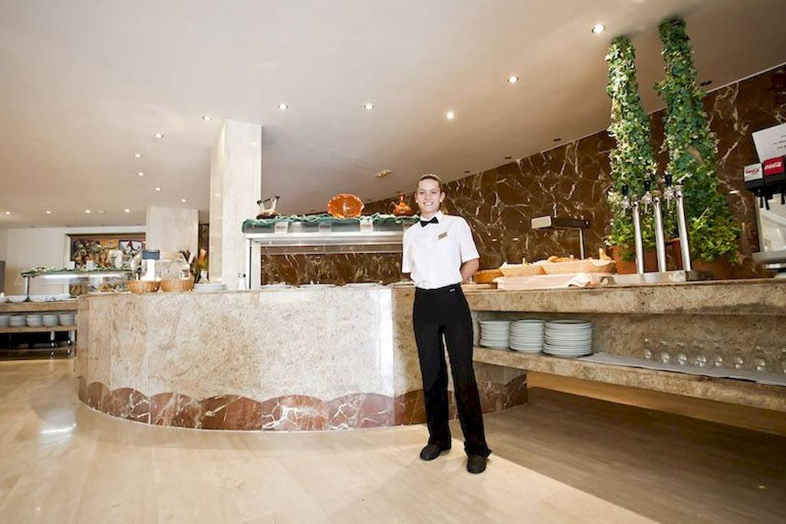 Ein Mitarbeiter im Restaurant des Playa Dorada Aparthotel, das mit Marmor und Holz gestaltet ist.