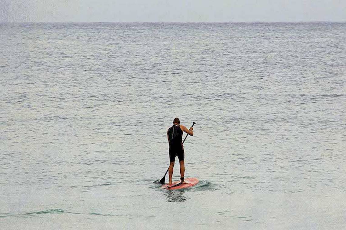 Ein Mann steht auf einem roten Surfbrett und paddelt auf dem offenen Meer.