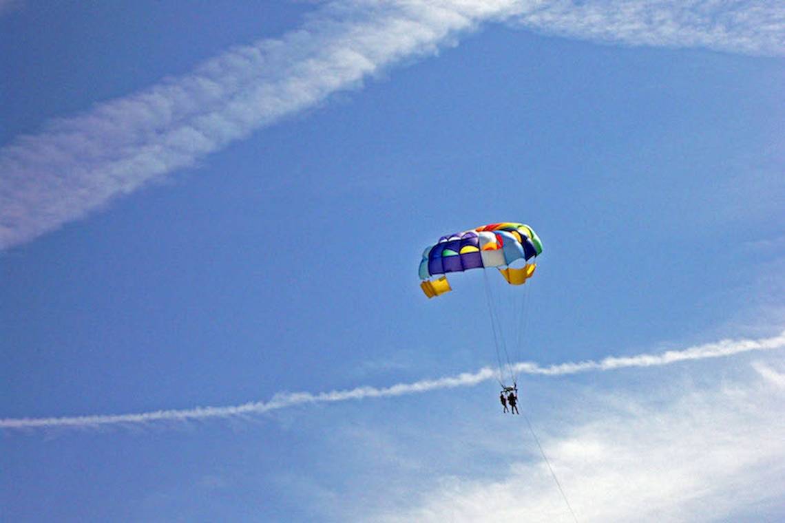 Zwei Personen parasailing in einem farbenfrohen Fallschirm am Himmel.
