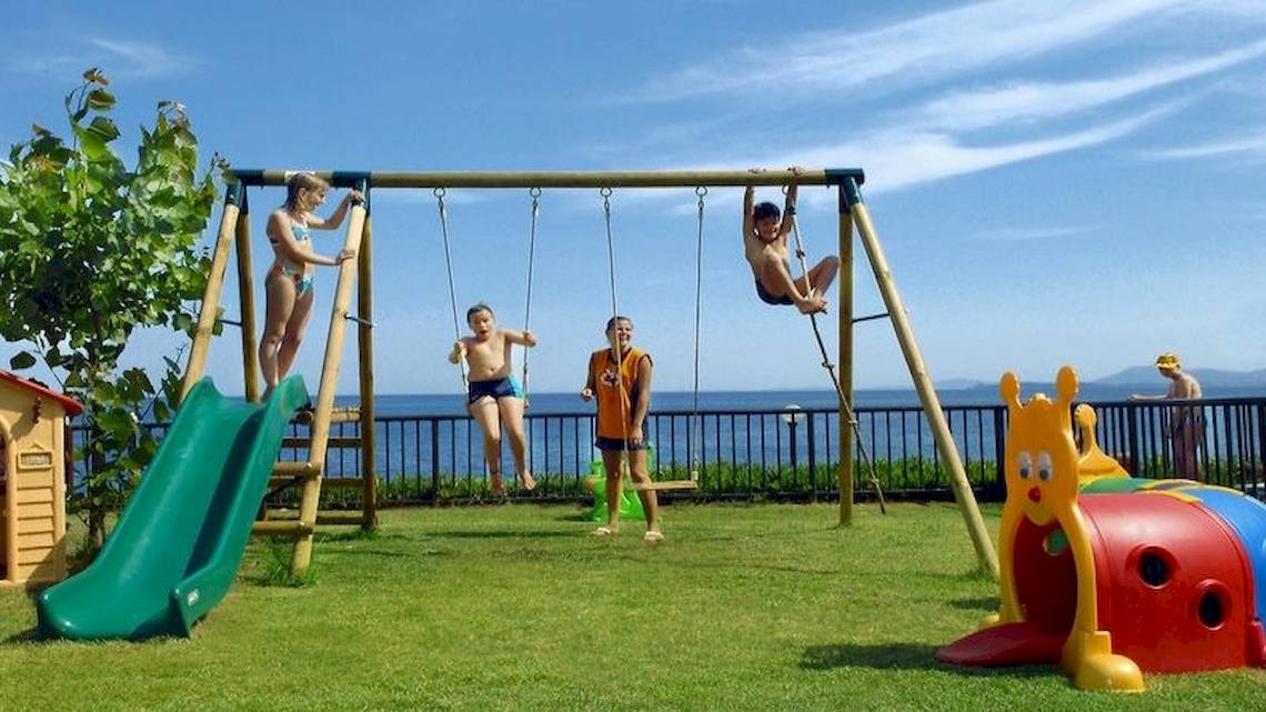 Kinder spielen auf einem Spielplatz im Freien im Atlantica Nissaki Beach Hotel.